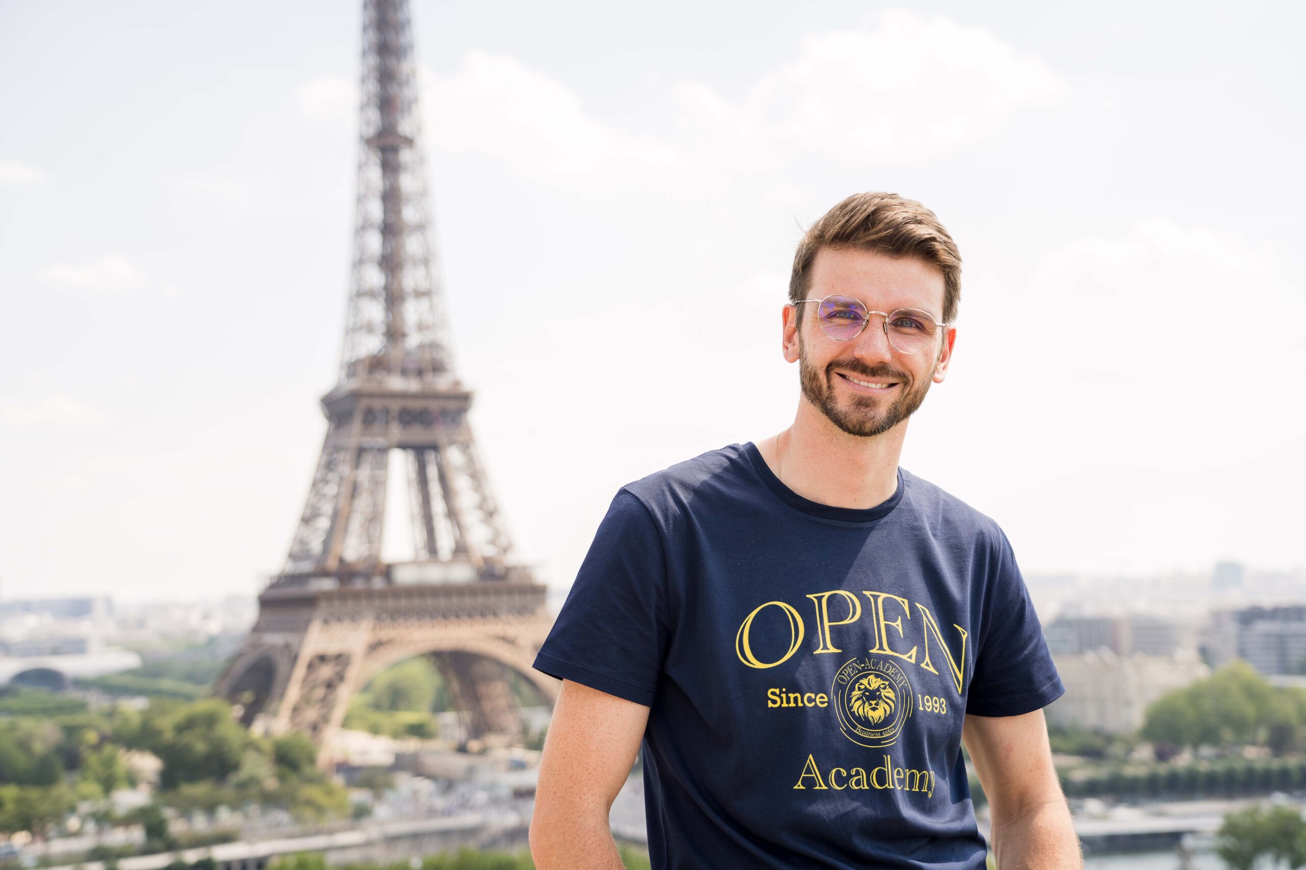 Homme avec des lunettes pose devant le tour Eiffel
