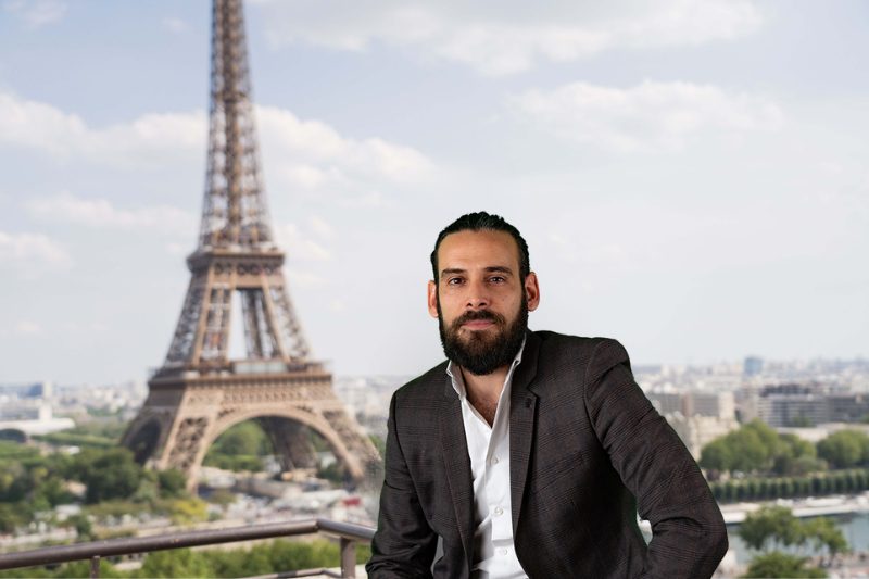 Un homme en costume et cravate assis devant la tour Eiffel.