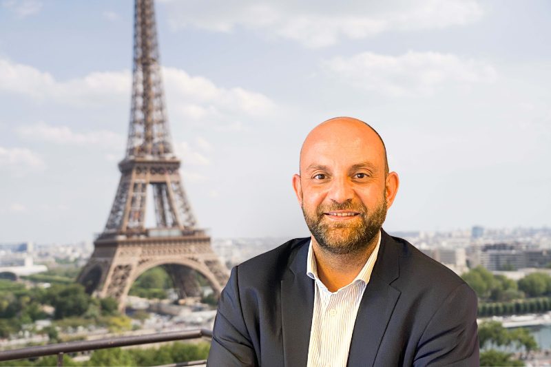 Un homme chauve en costume et cravate assis devant la tour Eiffel