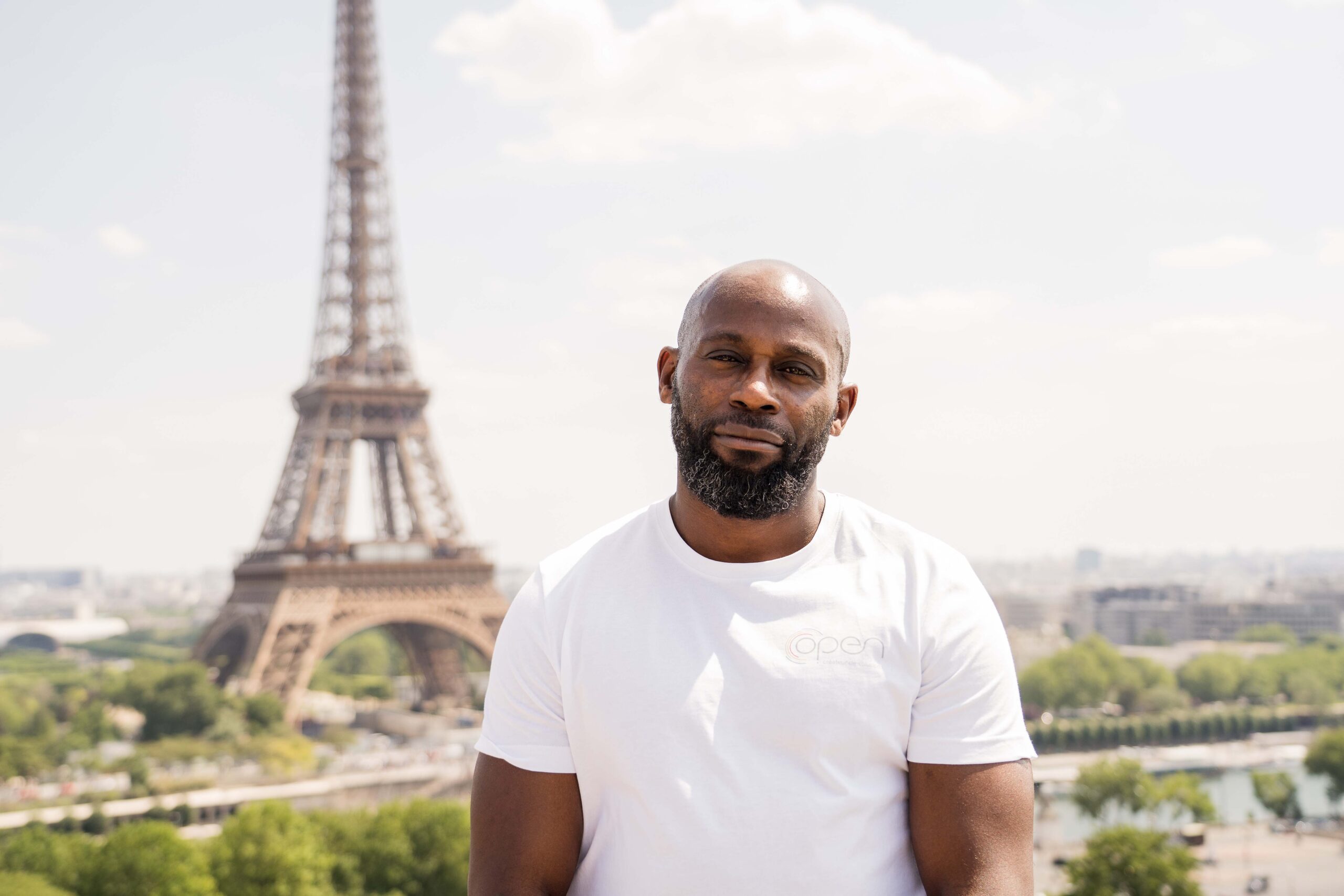 Un homme en t-shirt blanc devant la tour Eiffel.