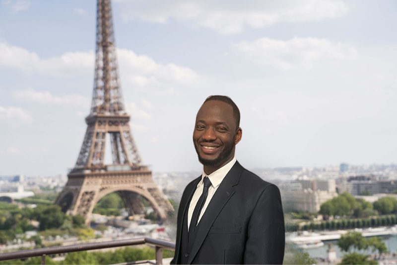 Un homme en costume et cravate se tenant devant la tour Eiffel.