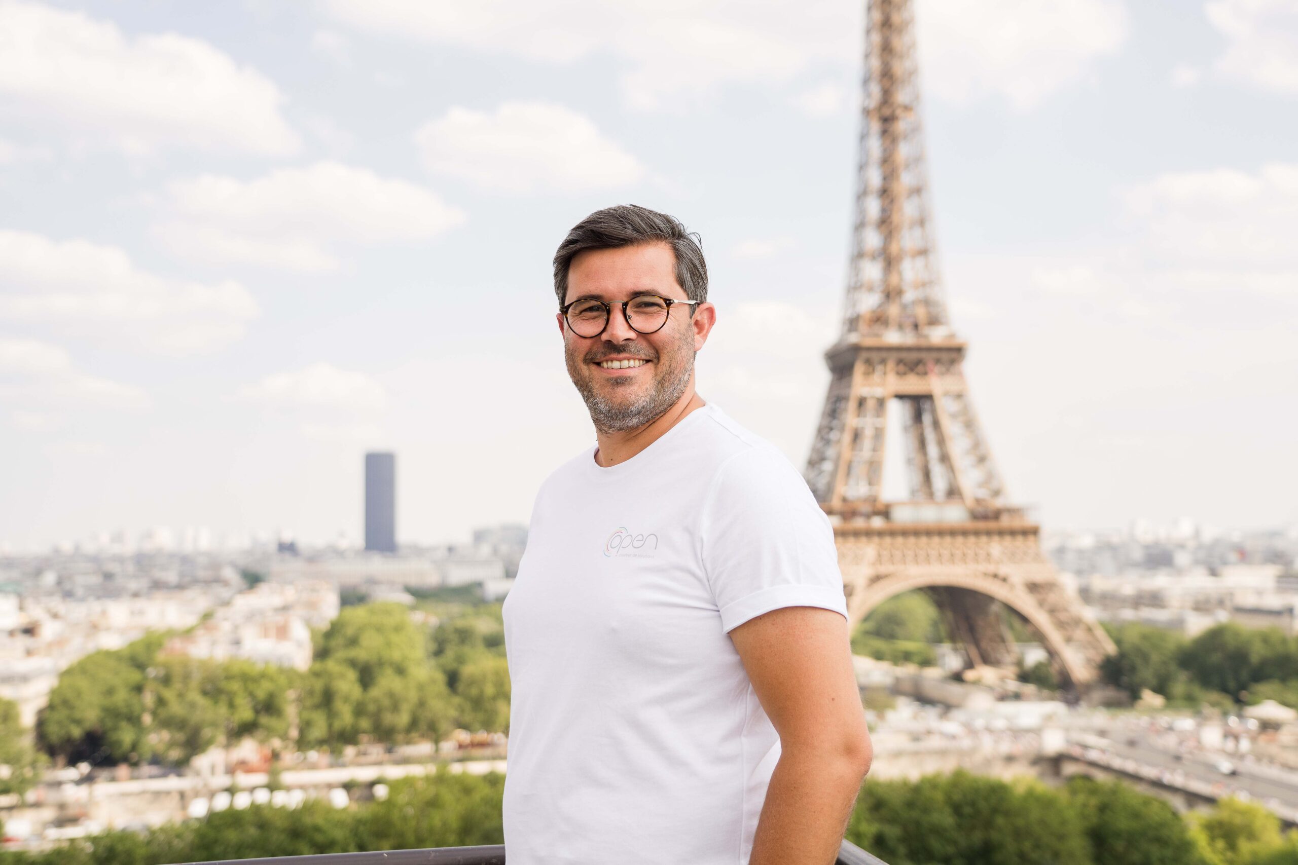 Un homme à lunette se tenant devant la tour Eiffel