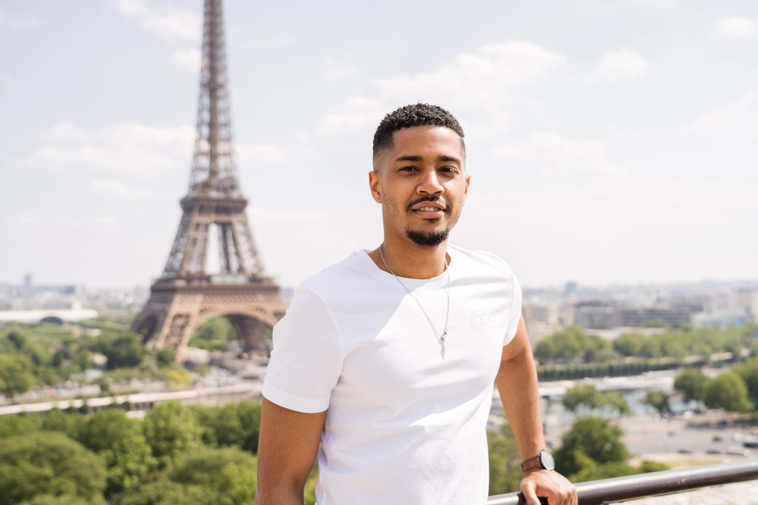 Jeune homme en tee shirt blanc devant la tour Eiffel.