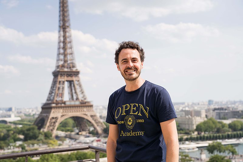 Un grand homme avec un tee-shirt bleu face à la Tour Eiffel
