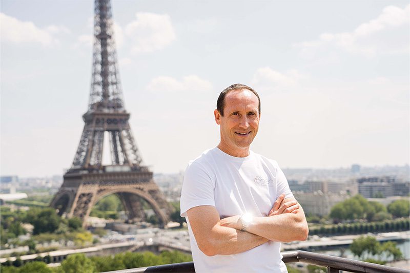 Un homme debout vêtu d'un tee shirt blanc devant la Tour Eiffel