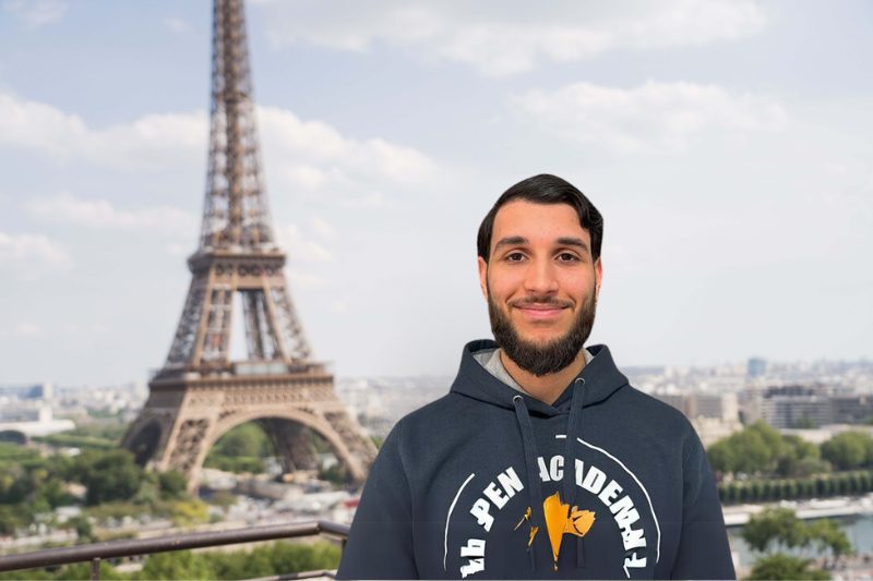 Un homme portant un sweat à capuche se tient devant la tour Eiffel.